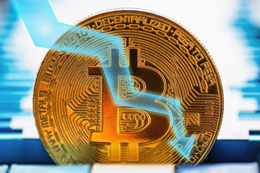 Zlatá minca Bitcoin - symbol kryptomeny a šípka smerujúca nadol na technickom pozadí.