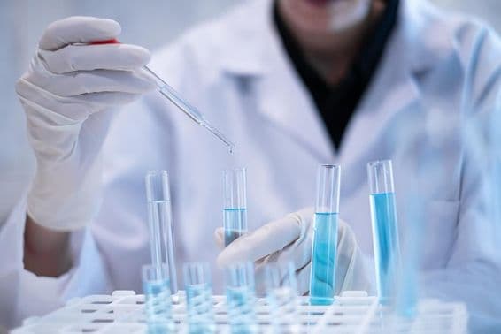 Vedec pipetuje modrú kvapalinu do skúmavky v laboratóriu.