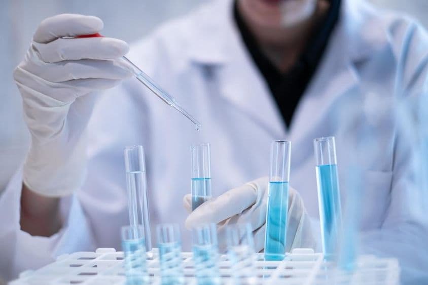 Vedec pipetuje modrú kvapalinu do skúmavky v laboratóriu.