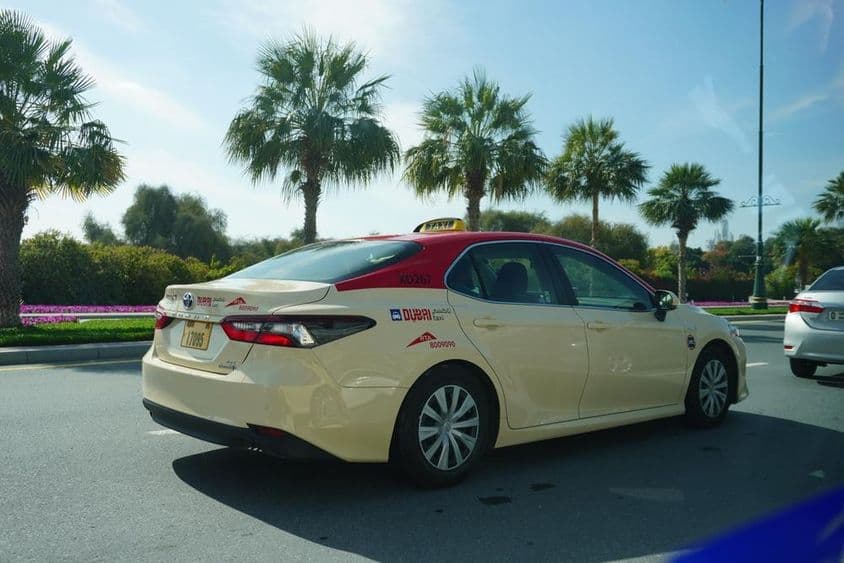 Dubajský taxík s červenou strechou jazdiaci po ceste.