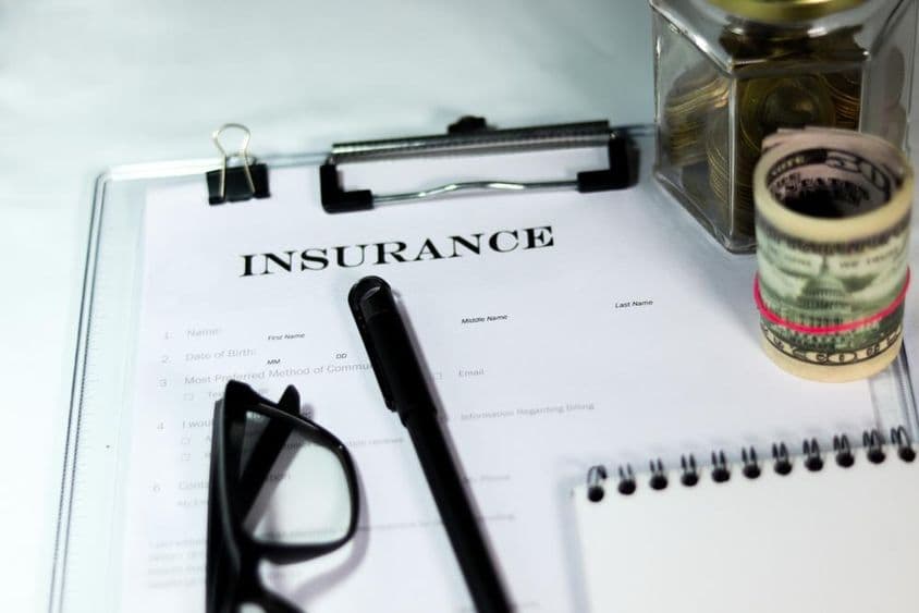 Formulár poistenia s pokladničkou, balíkom dolárov, perom a okuliarmi.