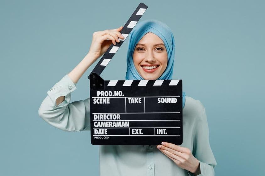 Mladá arabská moslimská žena v abáji hijabe držiaca klasickú čiernu filmovú klapku.