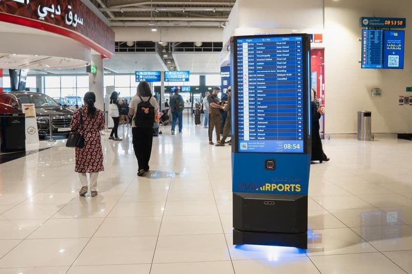 Interiér dubajského letiska s informačnou tabuľou.