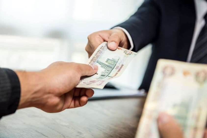 Podnikateľ odovzdávajúci peniaze v mene SAE dirham obchodnému partnerovi.