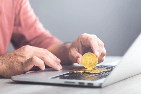 Muž držiaci zlatý Bitcoin pri používaní laptopu.