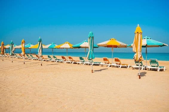 Dubajská verejná pláž, piesočný breh, slnečníky a modré more.