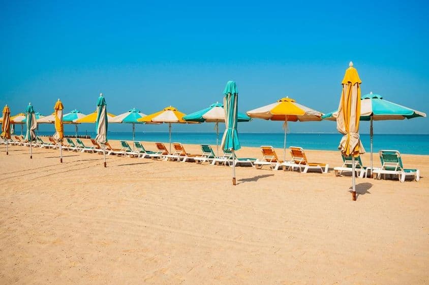 Dubajská verejná pláž, piesočný breh, slnečníky a modré more.