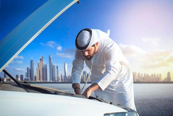 Arabský muž kontrolujúci svoje auto so zdvihnutou kapotou.