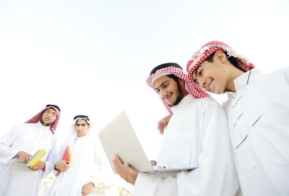 Šťastní arabskí študenti sledujúci vzdelávací obsah na notebooku.