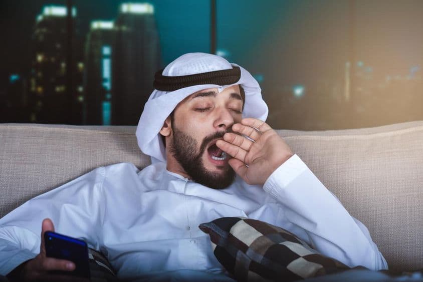 Arab muž zívajúci pri sledovaní televízie.