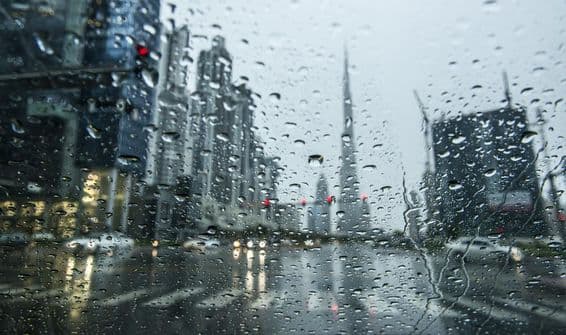 Dážď v Dubaji, rozmazaný pohľad cez daždivé okno, siluety Burj Khalifa v pozadí.