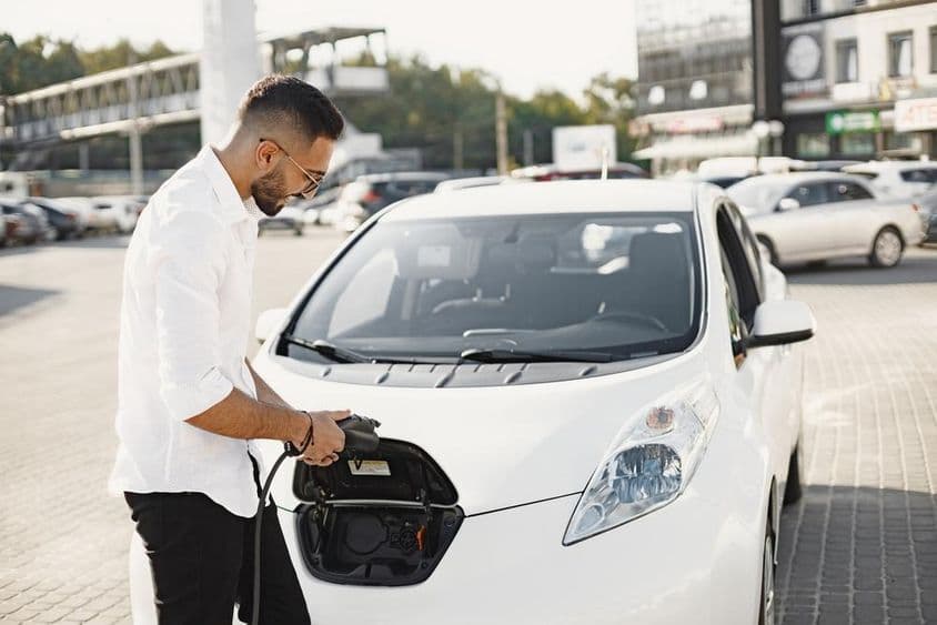 Mladý Arab nabíja biele elektrické auto.