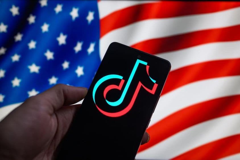 Logo TikToku zobrazené na smartfóne s americkou vlajkou v pozadí.