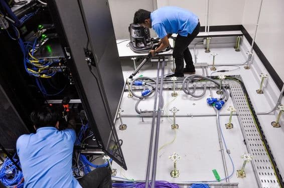 Pracovníci stavajú serverovú miestnosť, vyvýšená podlaha a rackové skrine.