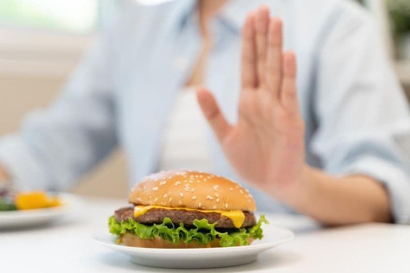 Žena odmieta hamburger z rýchleho občerstvenia s vysokým obsahom tuku.