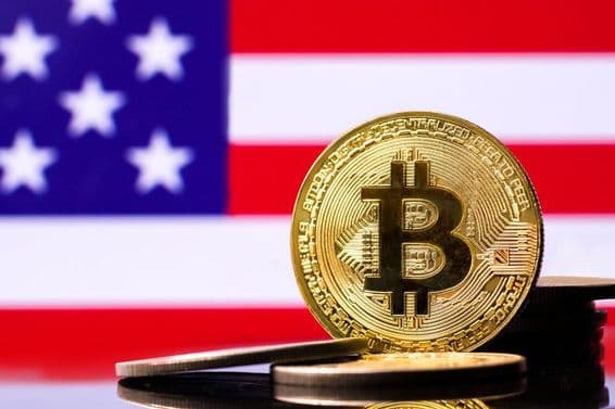 Zlatá kovová minca Bitcoinu s vlajkou USA v pozadí.