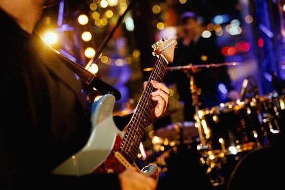 Gitarista hrá akord na hmatníku počas vystúpenia kapely.