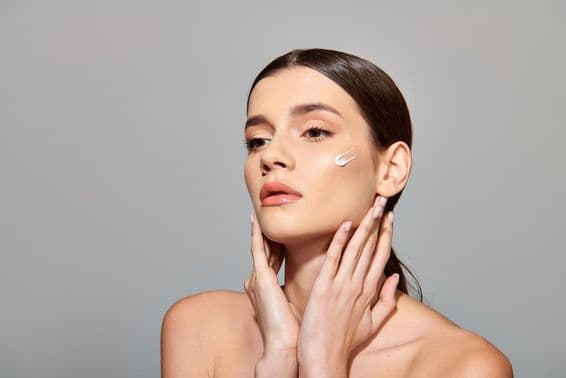 Mladá žena s hnedými vlasmi nanáša na tvár krém a vyžaruje pocit starostlivosti o seba.