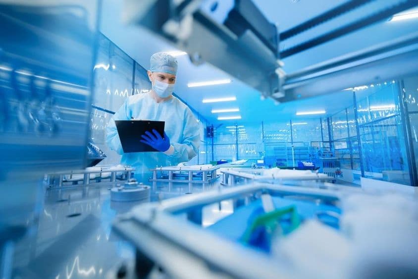 Farmaceutický pracovník obsluhujúci výrobnú linku v farmaceutickom priemysle.