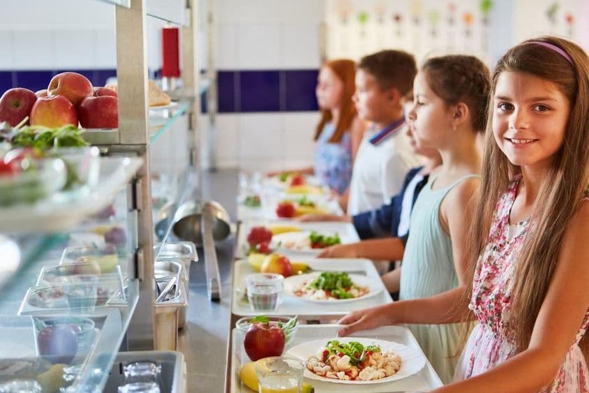 Usmievavé dievča s táckou na jedlo stojace v rade s priateľmi počas obednej prestávky v školskej jedálni.