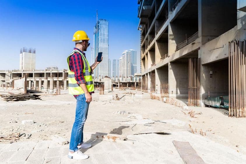 Smartfón, ochranná prilba a reflexná vesta pod panorámou Dubaja, stavebný pracovník.