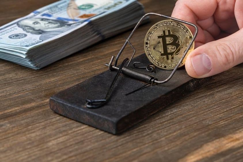 Kryptomenové mince Bitcoin v pasci na myši s uväznenými 100-dolárovými bankovkami.