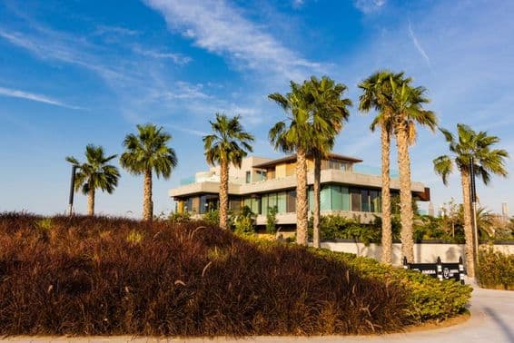 Dubaj, vila obklopená palmami na pozadí zamračeného západu slnka.