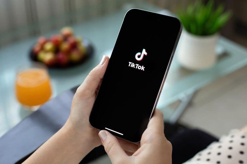 Apple iPhone 15 Pro Max v ruke ženy, TikTok video na obrazovke.
