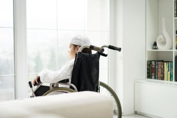 Mladý chlapec na vozíčku pozerajúci sa cez okno.