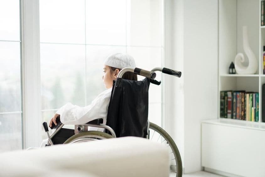 Mladý chlapec na vozíčku pozerajúci sa cez okno.