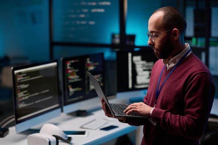 Počítačový programátor držiaci otvorený notebook v kancelárii IT a kybernetickej bezpečnosti.