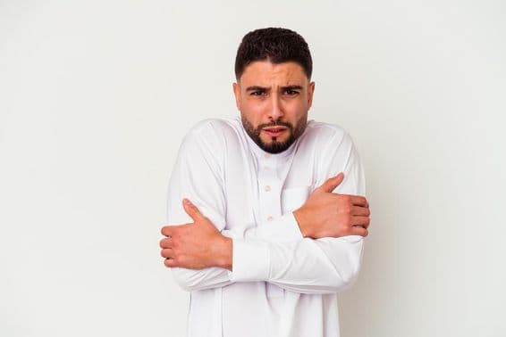 Mladý arabský muž v tradičnom oblečení trasúci sa od zimy.