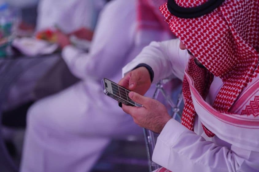 Arab muž pracujúci na mobilnom telefóne, čítajúci alebo písajúci správu.