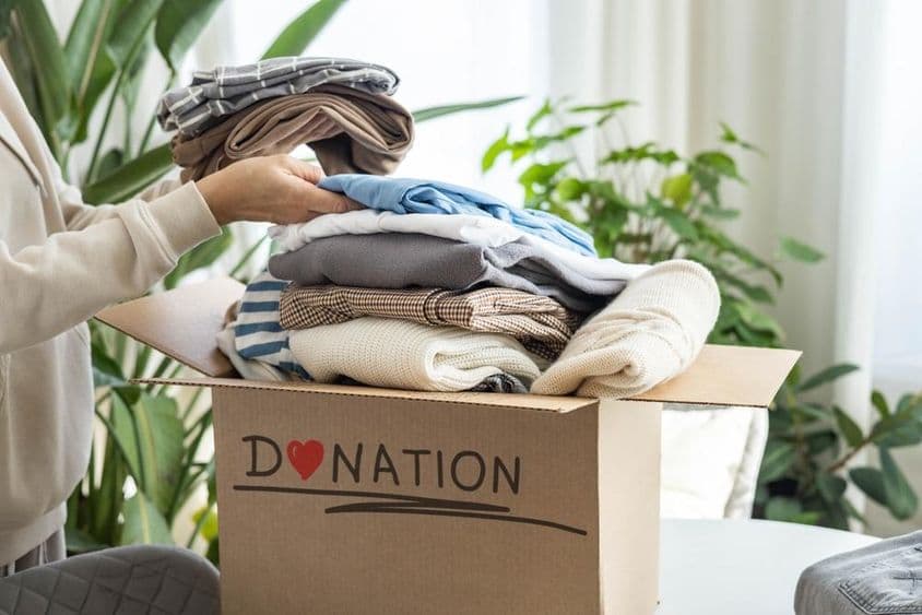 Žena doma ukladá oblečenie do kartónovej škatule na darovanie, na recykláciu.