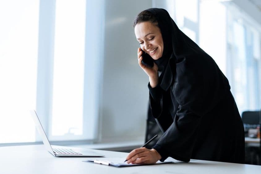 Krásna žena v abáje pracujúca na počítači a telefonujúca.