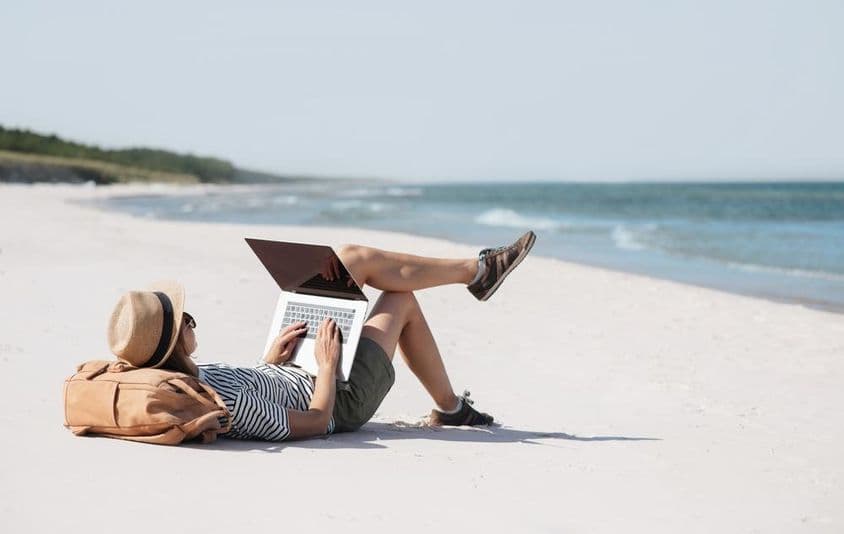 Mladá žena pracujúca na prenosnom počítači pri mori v rámci freelancingu.