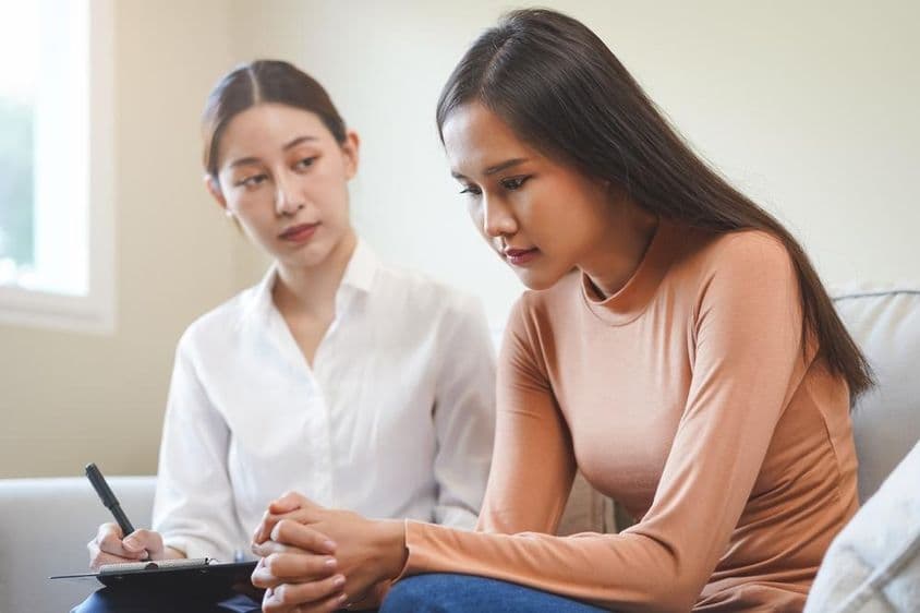 Smútna ázijská mladá žena konzultujúca s psychológom.