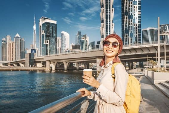 Moslimská žena so žltým batohom kráča popri dubajskom kanáli.