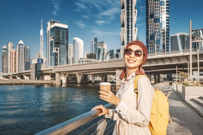 Moslimská žena so žltým batohom kráča popri dubajskom kanáli.