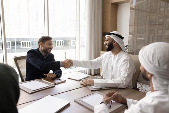 Multinacionálni obchodní partneri uzatvárajú úspešnú dohodu s podaniem rúk.