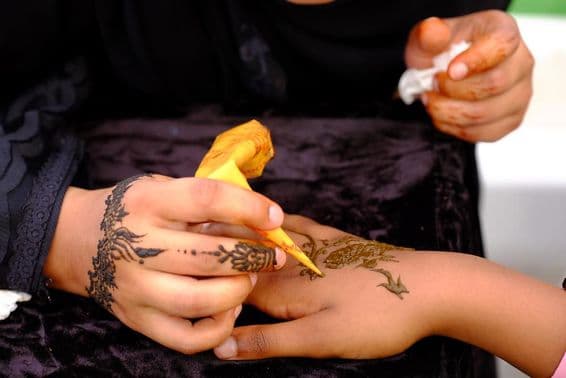 Dievča nanášajúce henna vzor na ruku inej.