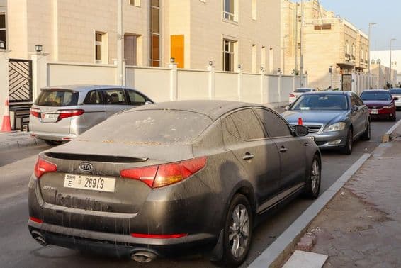 Prašné a pieskom pokryté autá s dubajskou poznávacou značkou zaparkované v Abú Zabí.