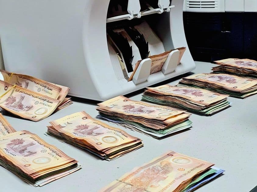 Počítačka meny s bankovkami emirátskeho dirhamu úhľadne usporiadanými na stole