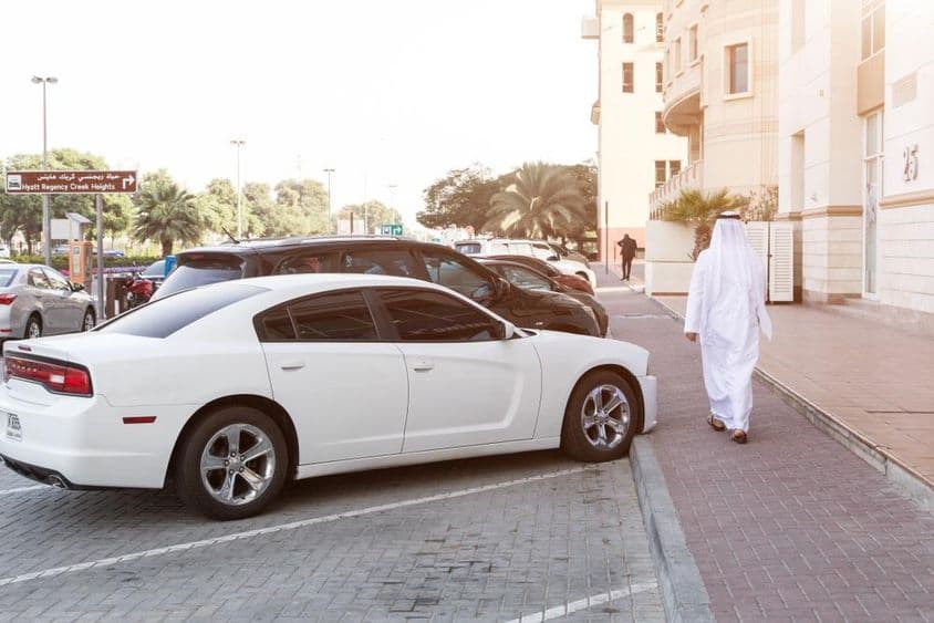 Na uliciach Dubaja: Muž v národnom kroji a biely Dodge na parkovisku.