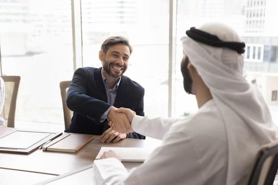 Usmiaty obchodník podáva ruky arabskému partnerovi.