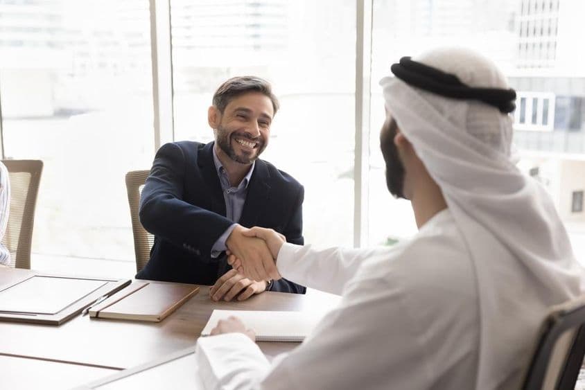 Usmiaty obchodník podáva ruky arabskému partnerovi.