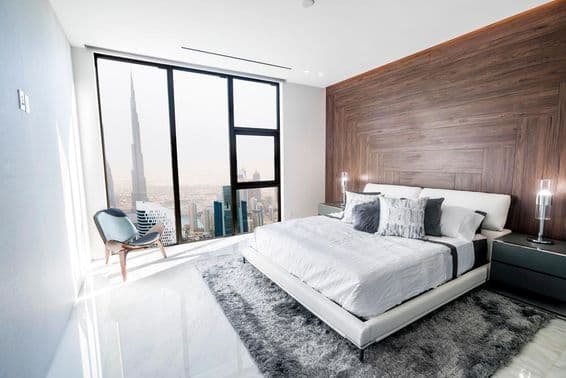 Luxusná spálňa s bielym stropom a drevenými lemovaniami, s výhľadom na centrum Dubaja.