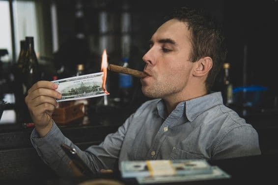 Mladý pohľadný muž si zapaľuje cigaru stodolárovkou v bare.