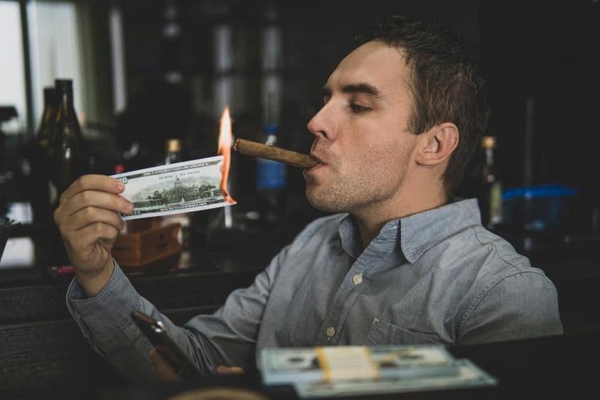 Mladý pohľadný muž si zapaľuje cigaru stodolárovkou v bare.