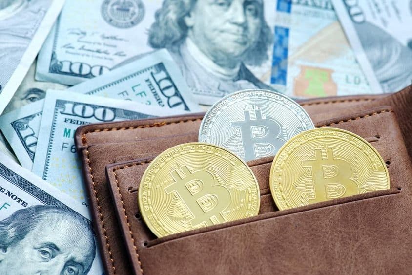 Zlatý bitcoin s peňaženkou, pod dolárovými bankovkami.